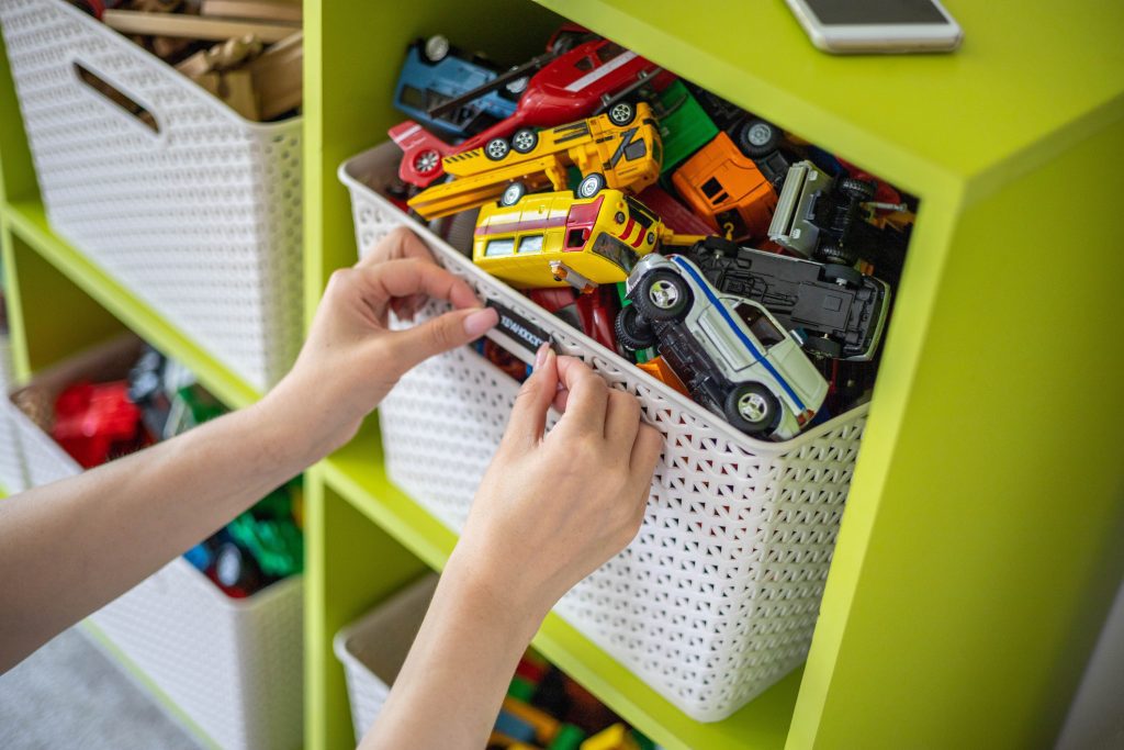 Woman hands applying printing sticker with name title of children toys for comfortable sorting and storage at home. Caring mother organizing domestic space for kids. Housekeeping and household home storage solution