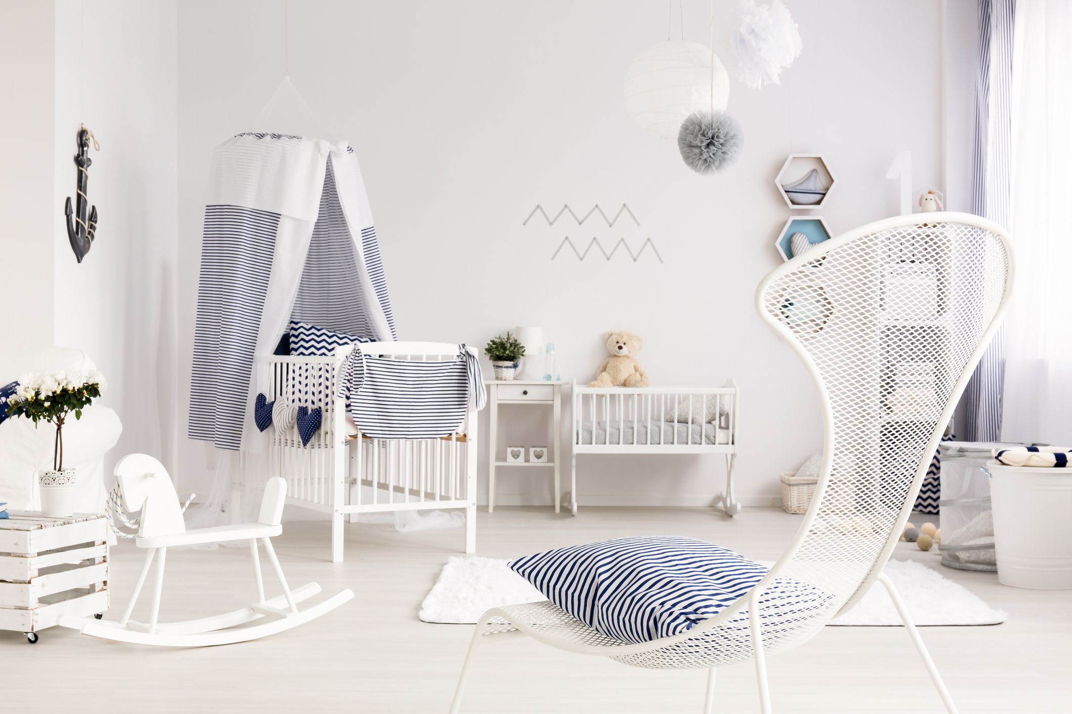 Bright and clean room for a newborn, with a wire armchair in the foreground and white baby room furniture