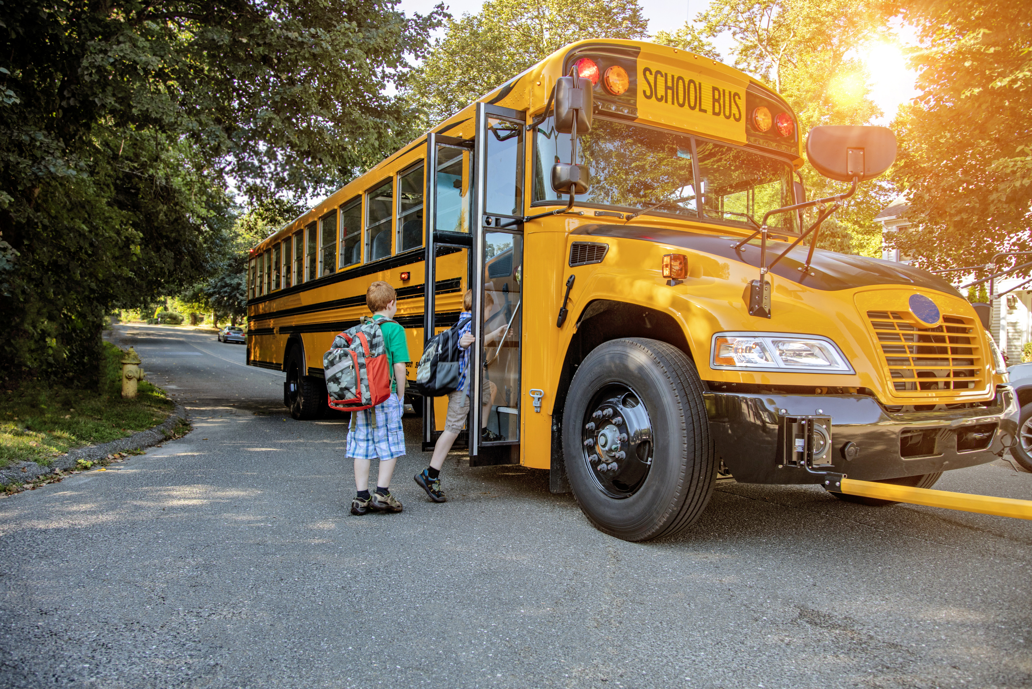 A young redheaded boy getting onto a school bus in sunshine in school district 