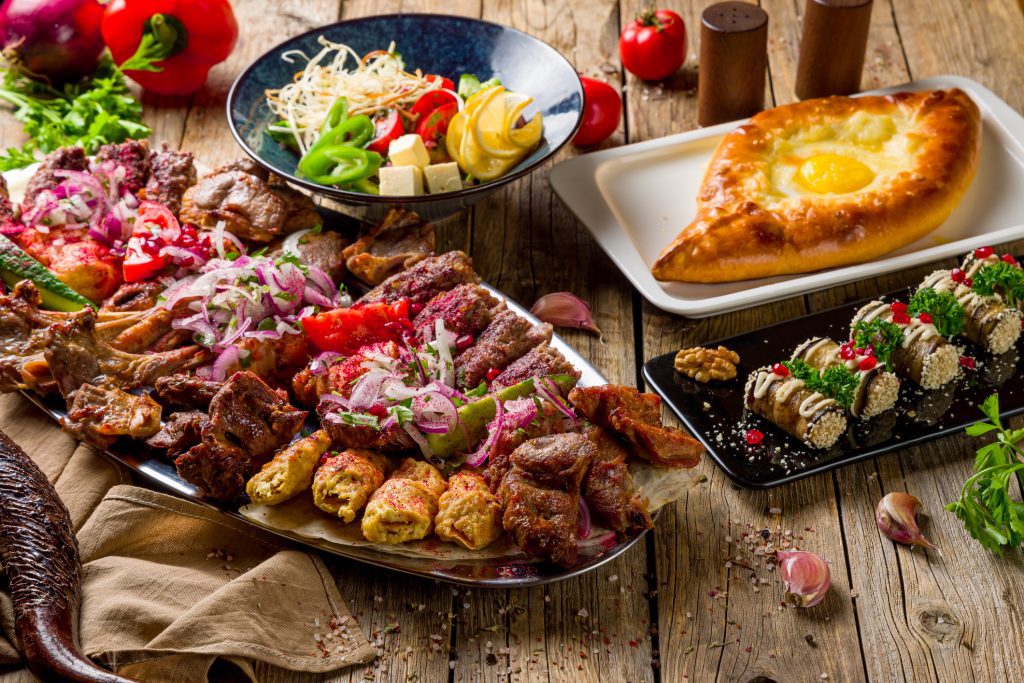 Georgia: platter of different kebabs, Adjara khachapuri, dolma and auberdine eggplant rolls with nuts on wooden table