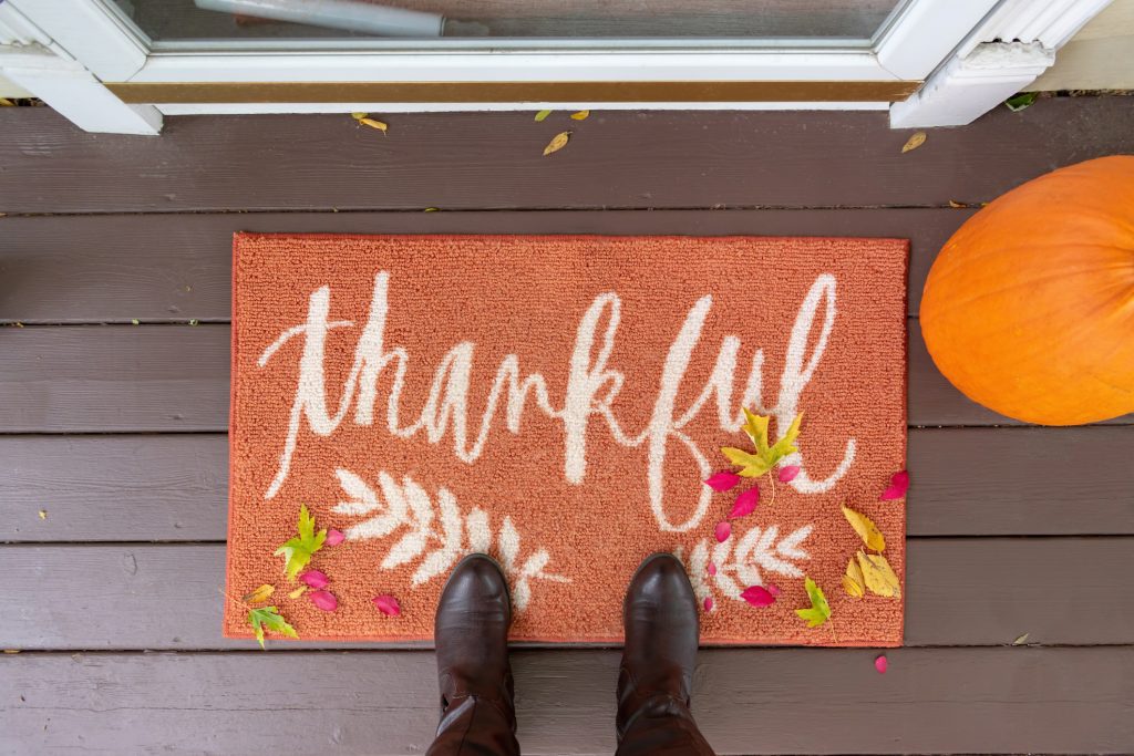 Welcome mat on the front porch with the word "thankful" with boots and fall leaves_fall real estate trends