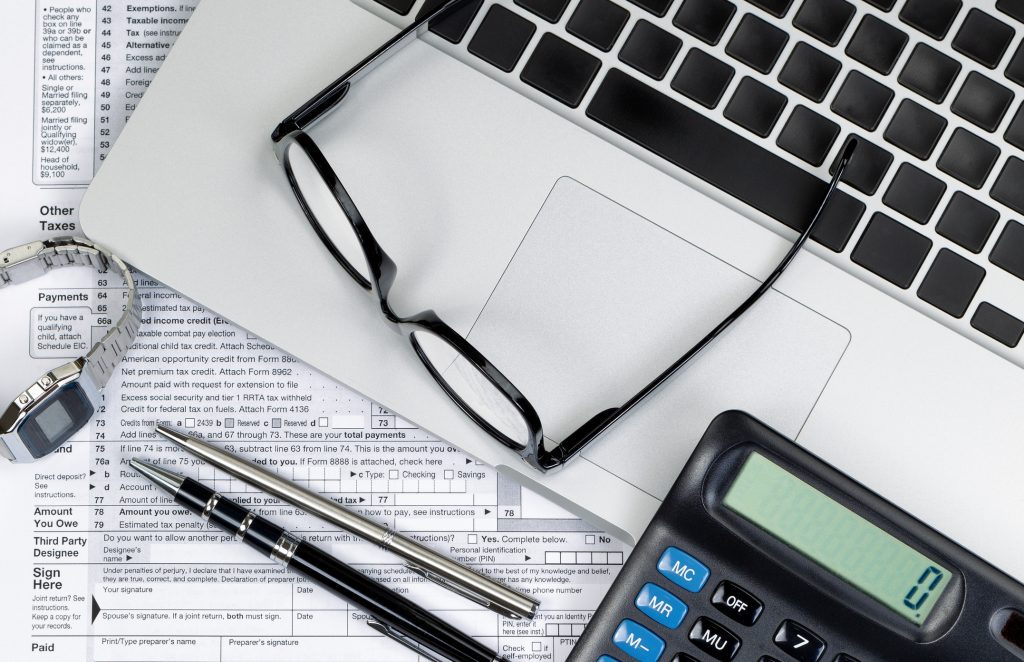 Tax form with laptop, reading glasses, wrist watch, pens, and calculator. Preparing income tax concept.