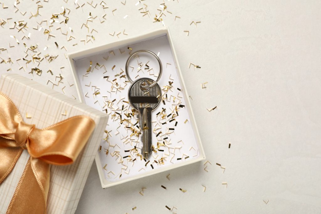 Key with confetti in gift box on white table, flat lay and space for text. Housewarming party