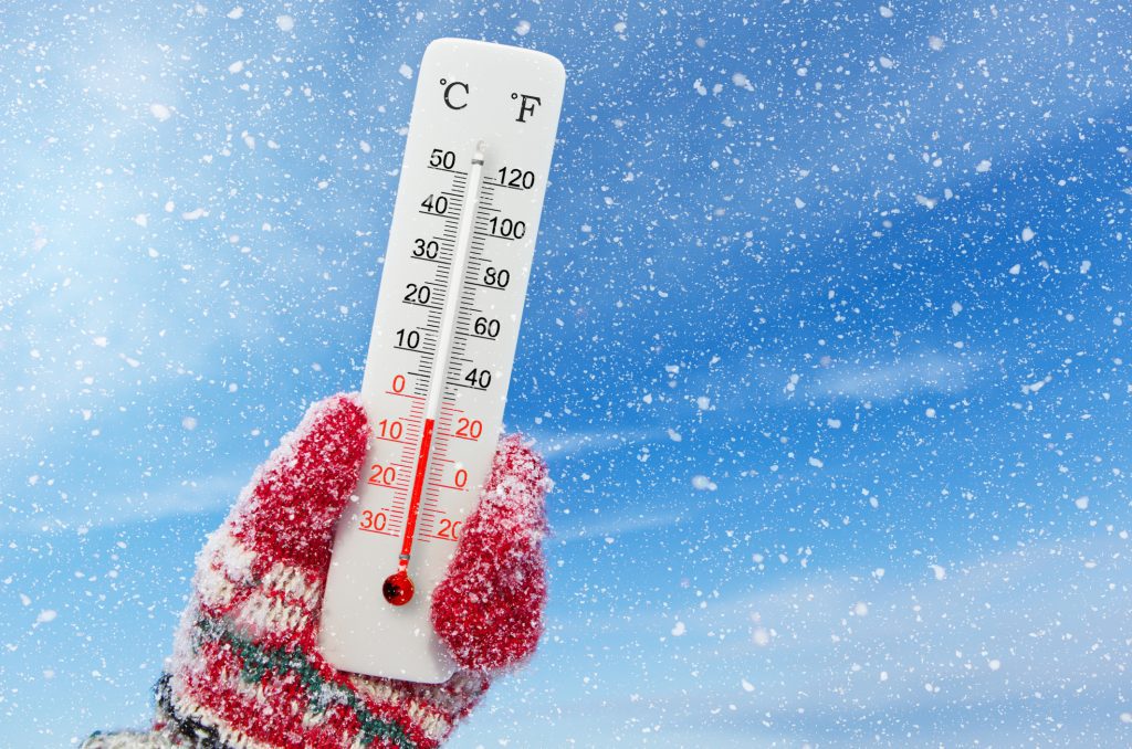 White celsius and fahrenheit scale thermometer in hand. Ambient temperature minus 4 degrees celsius. winter home maintenance tips